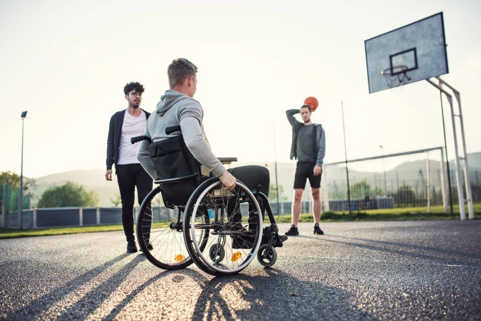 A disabled man sitting in his wheelchair playing basketball with 2 friends